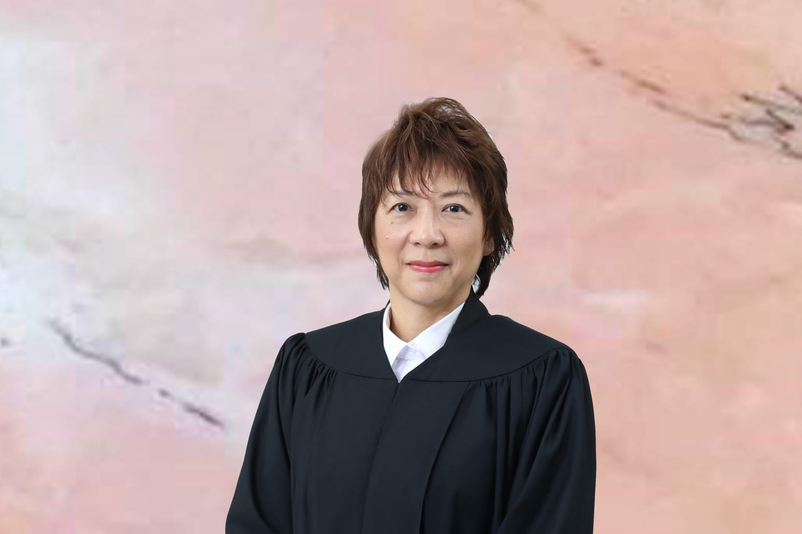 Person in judicial robe against mottled pink background.